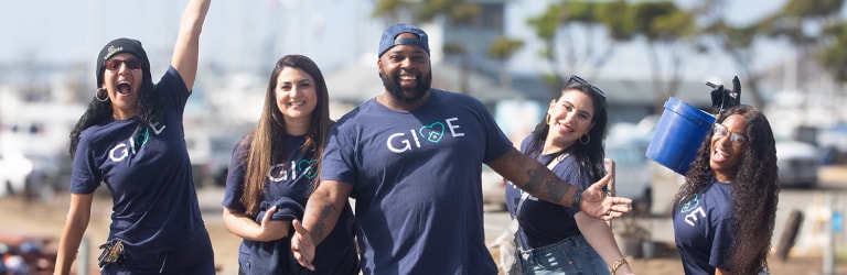 Five GID employees, wearing blue GIVE-branded T-shirts and carrying blue buckets, posing for a photo at a community volunteering event