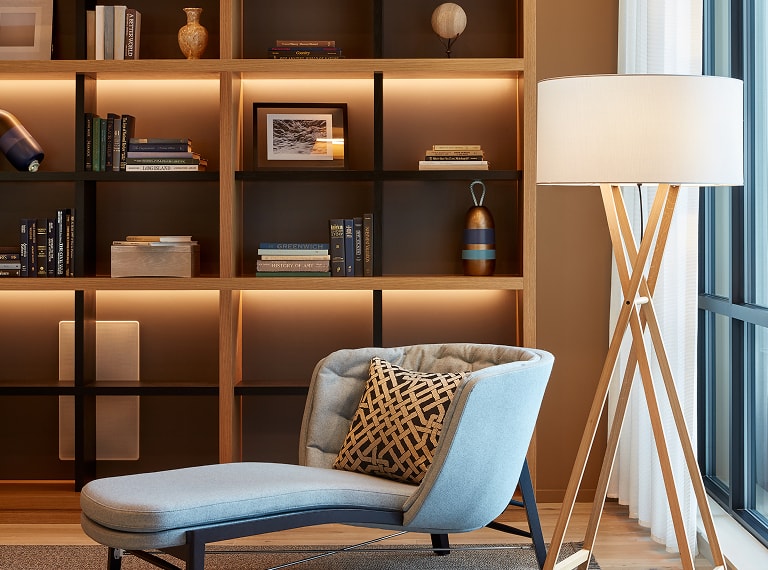 Modern residential interior with wooden shelving, books and decorative objects, a lounge chair and floor lamp