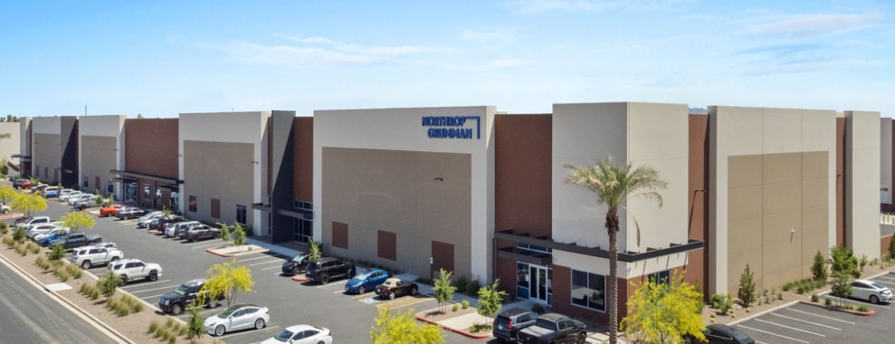 A rectangular building with palm trees and parked vehicles around the outside