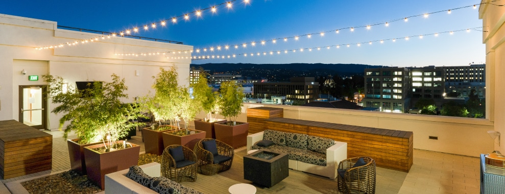 An outdoor patio area with cushioned seating arrangements around a square fire pit