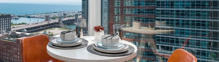 Table setting with two seats of white cups and saucers placed on a round table. The background is a view of a cityscape featuring a bridge and several buildings