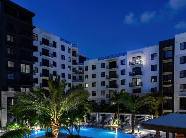 Centrico by Windsor, Doral, Florida. A multi-story building with a modern architectural design.Several palm trees are surrounding a swimming pool with lounge chairs