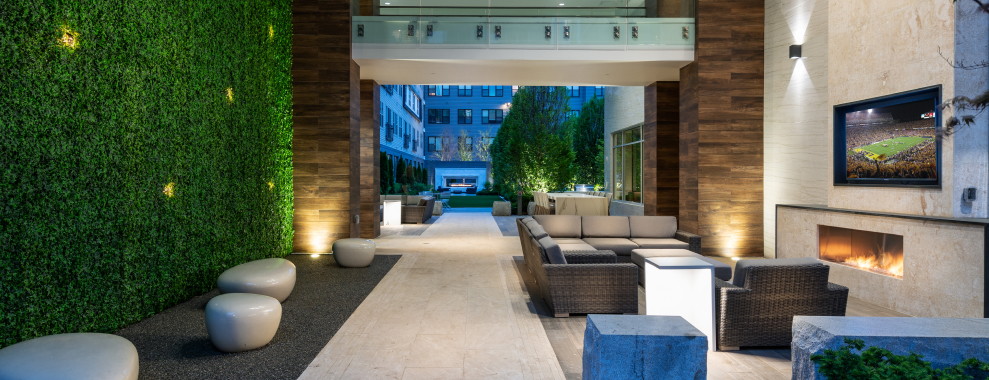 A modern outdoor space with a vertical green wall with embedded lights. A pathway in the center with a seating area on the side