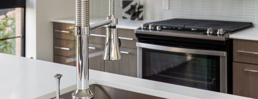 A kitchen faucet with oven in the background