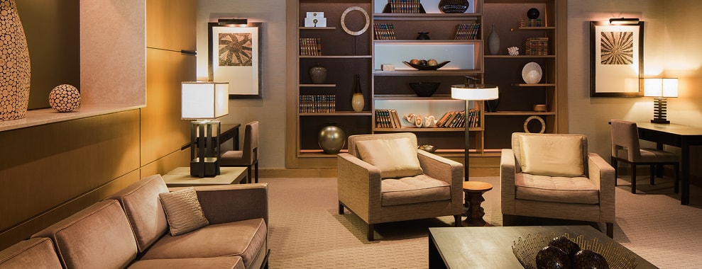 Modern residential interior with wooden shelving, books and decorative objects, lounge chairs, and floor and table lamps