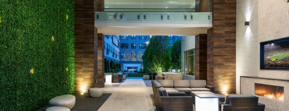 Modern atrium area with seating, a fireplace and a wall-mounted television, leading to an outdoor courtyard