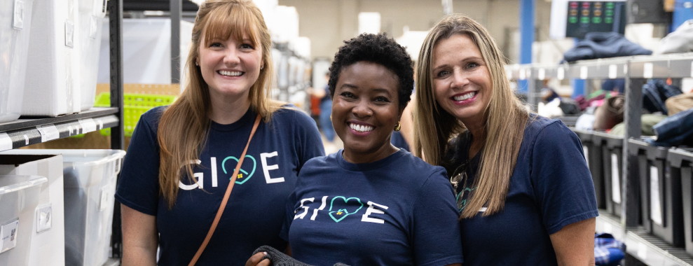 Three individuals all wearing matching navy blue shirts with the GIVE logo and heart symbol