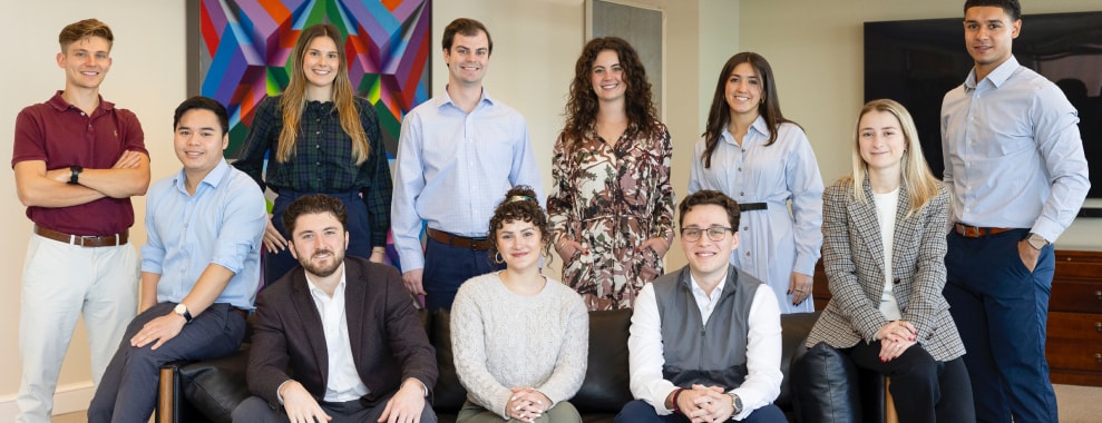 A group of 10 people posing for a photo, some sitting on a sofa and some standing behind, in an office setting