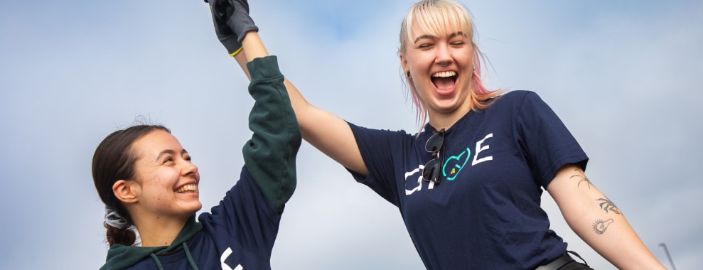 Two associates, wearing blue GIVE-branded T-shirts and gloves, celebrating outdoors