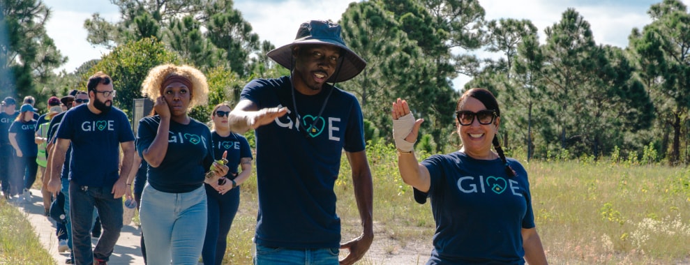 A group of people walking outdoors on a path, all wearing matching shirts with the word GIVE printed on them