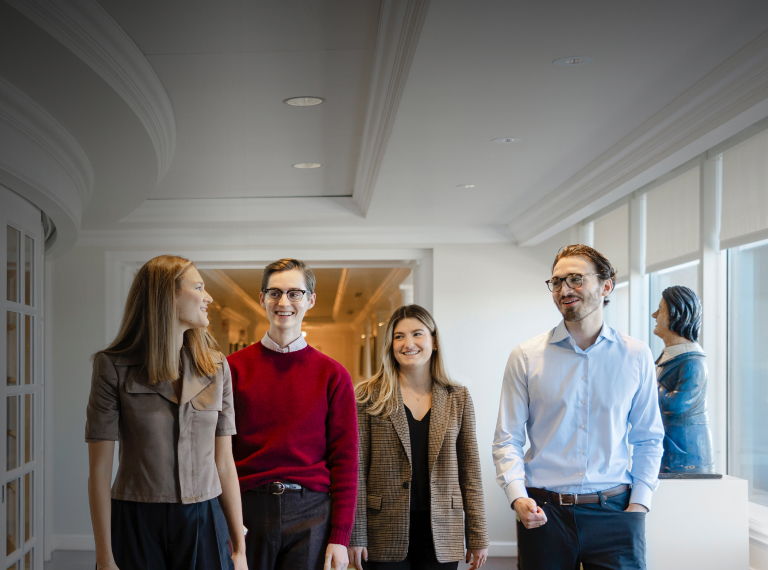 Four individuals walking in a row toward the camera in a light-colored interior space