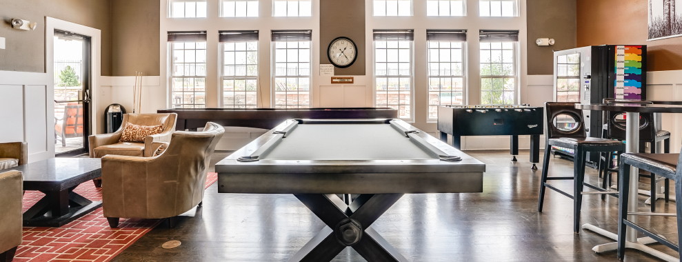 A light-colored interior with seating area, prominent pool table and other games, with large windows letting the light in