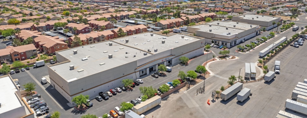 An aerial view of rectangular buildings with a flat roofs. Many vehicles are parked around the building