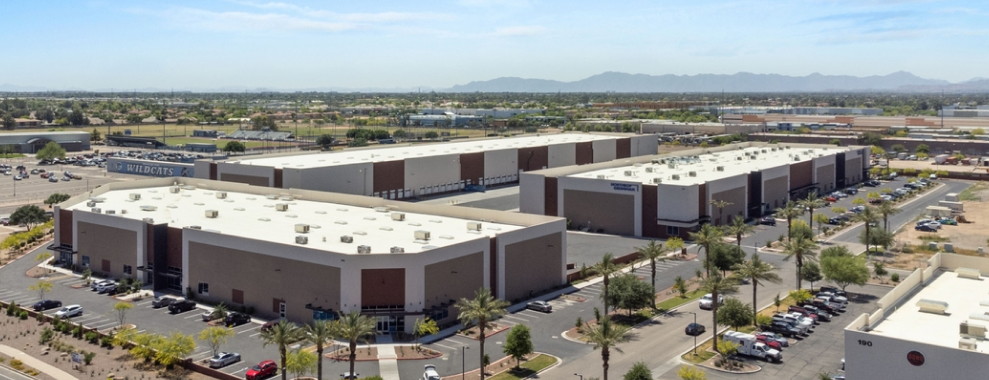 An aerial view of rectangular buildings with a flat roofs. Many vehicles are parked around the building