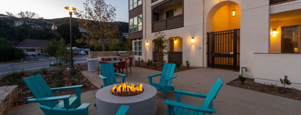 An outdoor seating area with several blue chairs arranged around a circular fire pit